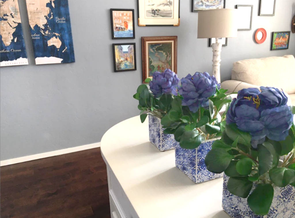 violet blue flowers in a pot with maps and artwork on the wall behind. modern farmhouse