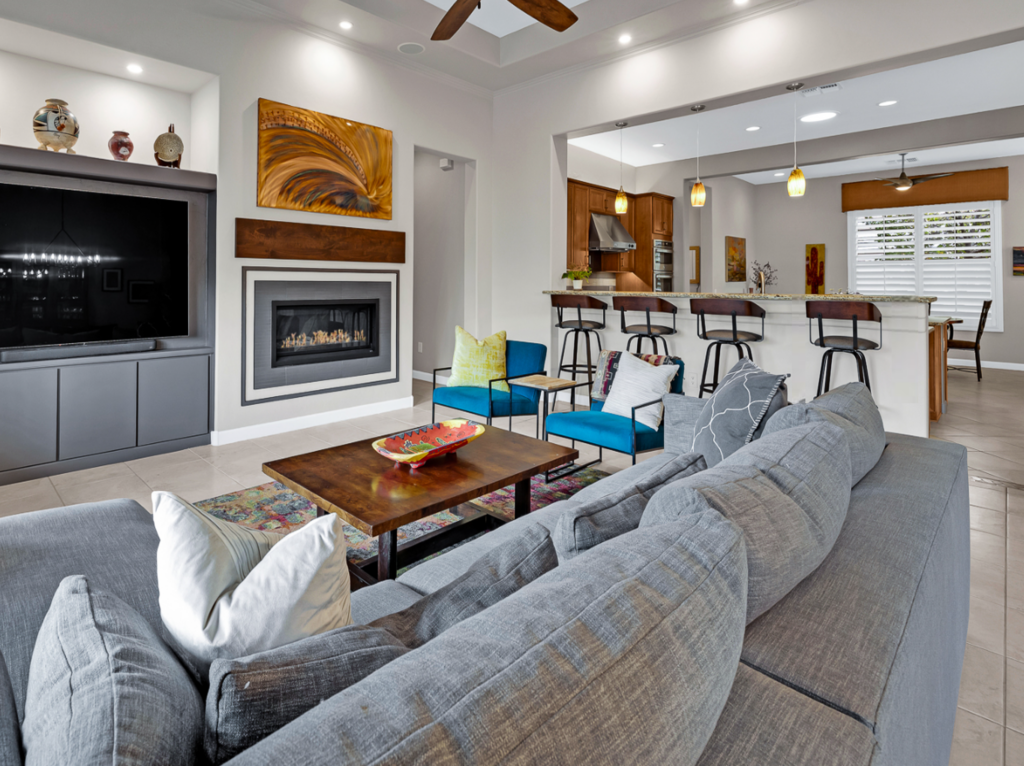 After Remodel with gray paint, linear fireplace with tile detail, tv alcove wood mantel, copper art gray wall, pendant lights.